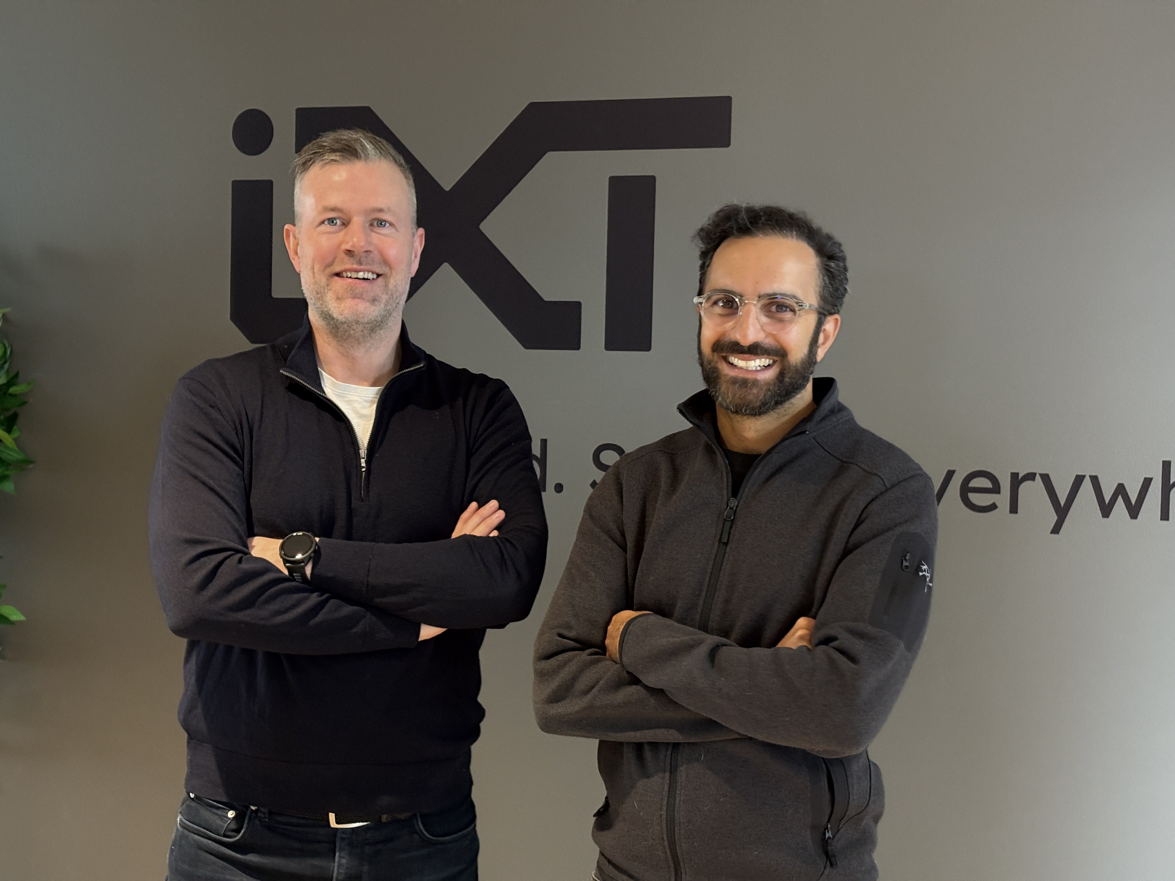 Raymond and Arvin from IXT smiling at the camera. Background is the ixt logo in black. 